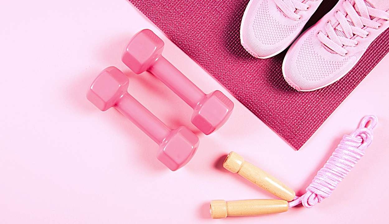 workout shoes, exercise mat, dumbbells' and skipping rope on a pink background
