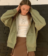 a girl wearing a white shirt under a sage green jacket and a brown skirt