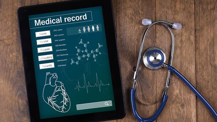 Medical record on tablet screen with stethoscope on wooden backg